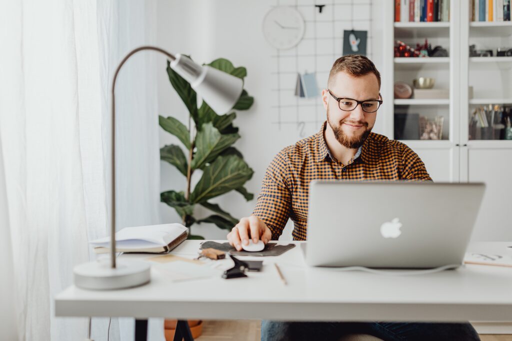 Best accounting software for e-commerce 2021 - man working on a laptop at a minimalist desk with a silver lamp and a green plant and bookcase in the background
