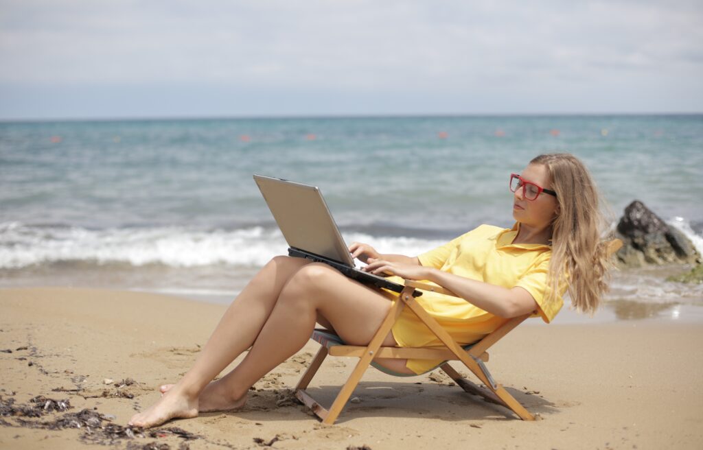 How to automate your e-commerce business - woman working on a laptop in a low deck chair, yellow sun dress, right by the ocean