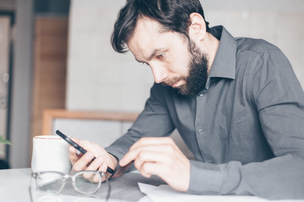 Square vs Stripe - Man in a grey shirt concentrating on his phone at a desk, glasses in the foreground