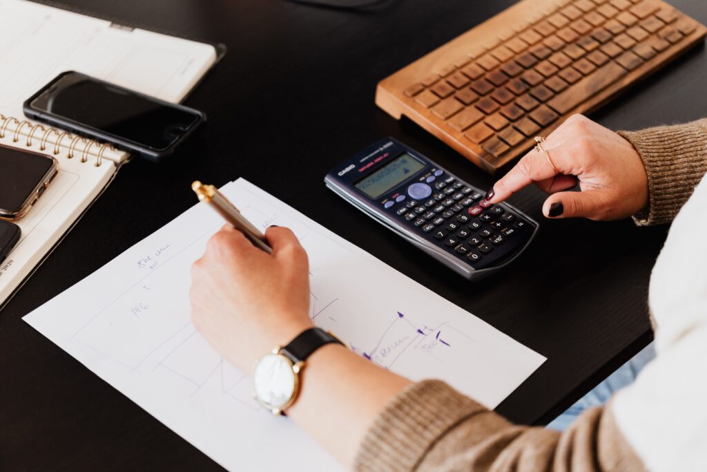 What are e-commerce accountants - woman using a calculator with her right hand and writing with her left on a black desk