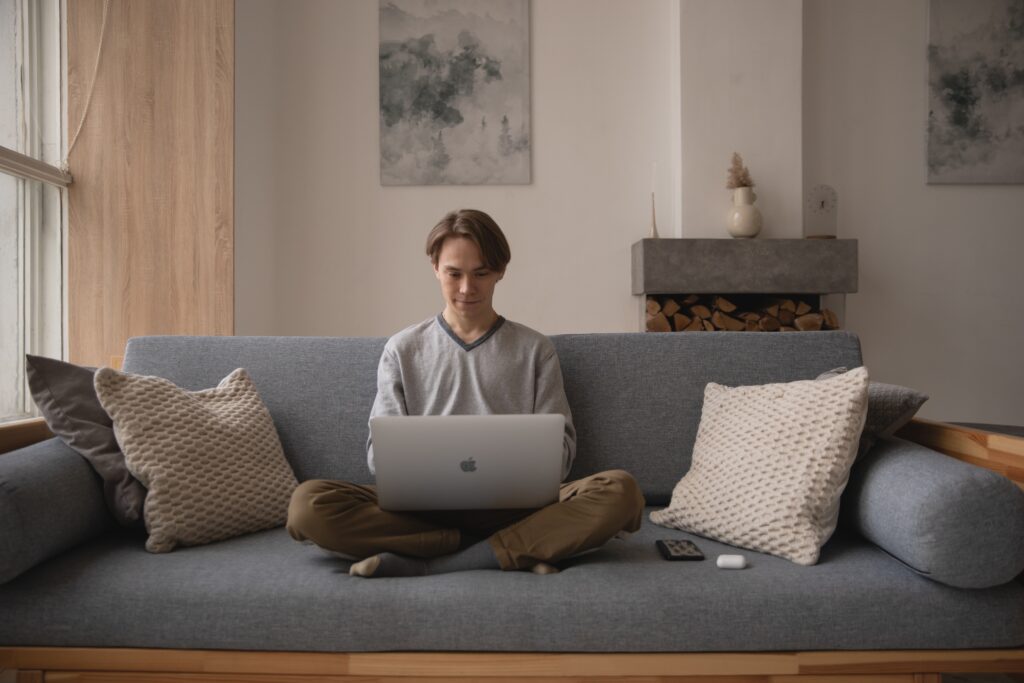 Register an e-commerce business - a man in casual clothes sitting cross-legged on a grey sofa working on a laptop