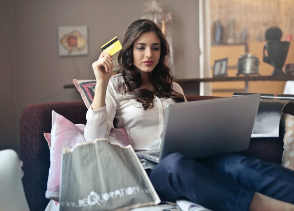 American Sales Tax for e-commerce entrepreneurs - woman with credit card in hand and laptop on her knee surrounded by shopping bags