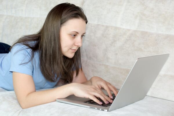 Do you pay VAT on eBay fees - lady in a blue tshirt working on a laptop lying on a bed