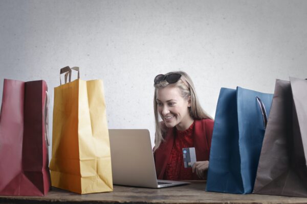 online vs high street shopping - woman sitting at laptop with a credit card surrounded by paper shopping bags