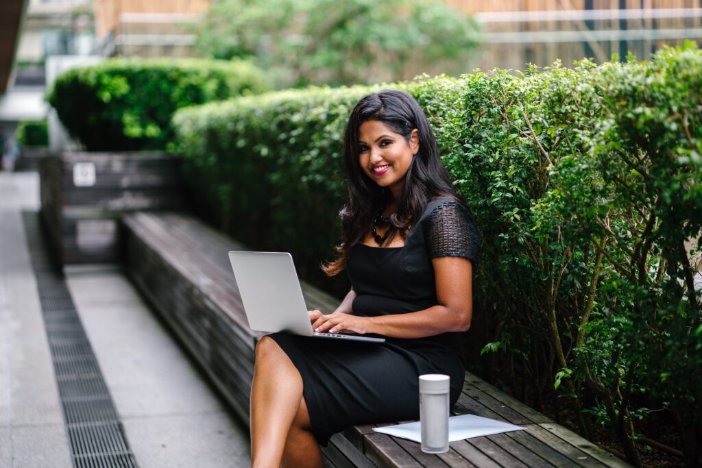 how to file a personal tax return - woman sitting on an outdoor bench next to a hedge with a laptop on her knee