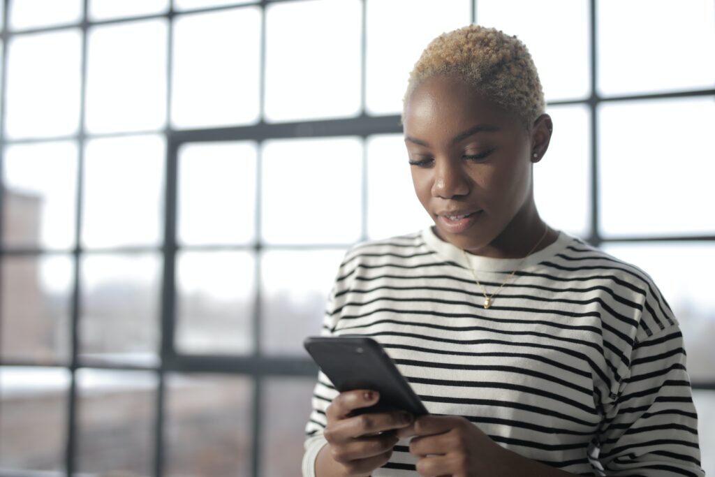 Notify my accountant - woman in a stripey top in front of a window looking at her phone