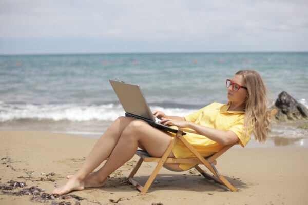 How to automate your e-commerce business - woman working on a laptop in a low deck chair, yellow sun dress, right by the ocean