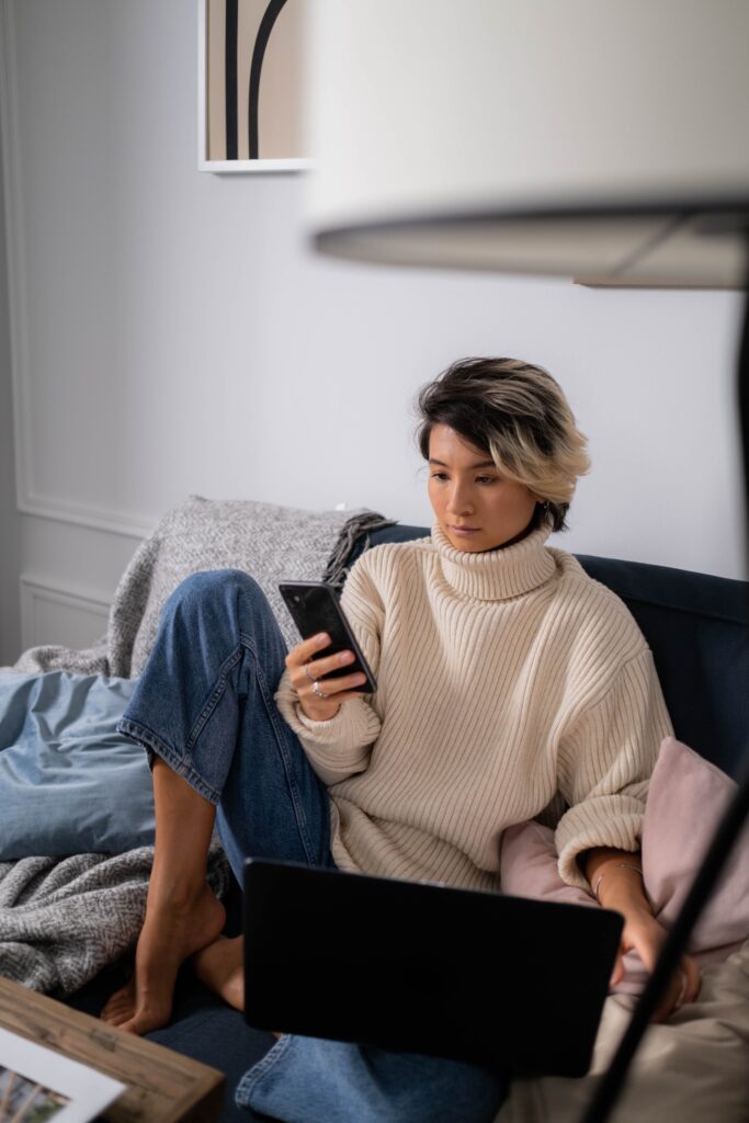 Most efficient way to pay yourself - woman in jeans and a big beige polo neck looking at her phone while lounging on a sofa