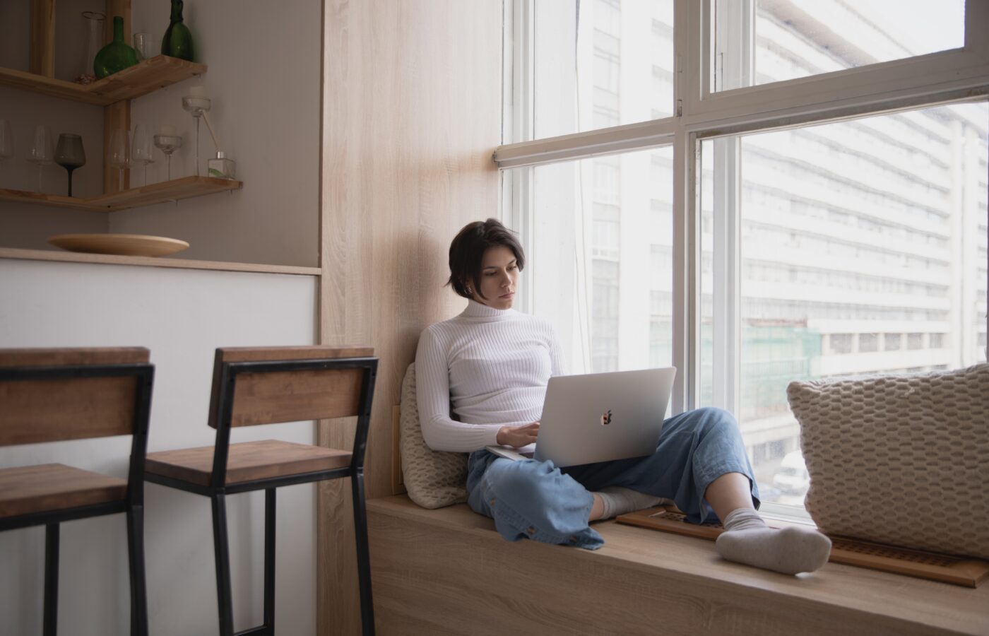 What is Xero Analytics Plus - woman in a white polo neck and jeans with short dark hard working in a window seat on a laptop