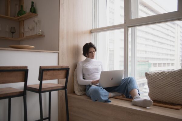 What is Xero Analytics Plus - woman in a white polo neck and jeans with short dark hard working in a window seat on a laptop