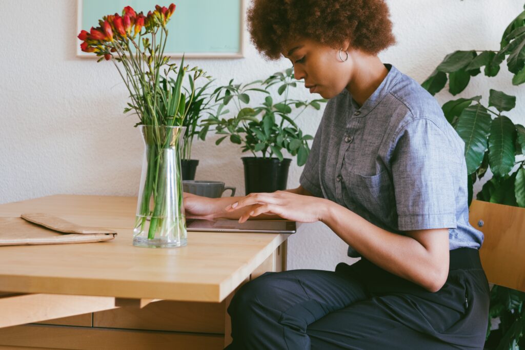 Amazon or own website - woman working on a tablet at a kitchen tablet with a vase of red flowers and a pot plant on it