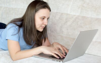 Do you pay VAT on eBay fees - lady in a blue tshirt working on a laptop lying on a bed