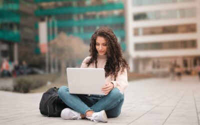 A2X vs Link My Books - lady in jeans and pink jumper sitting cross-legged on paement working on laptop