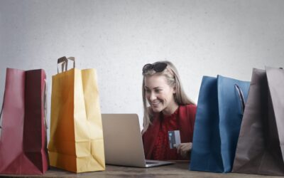 online vs high street shopping - woman sitting at laptop with a credit card surrounded by paper shopping bags