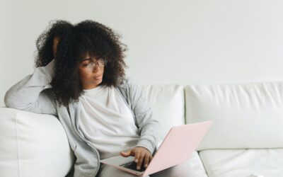 Syft for Xero - woman sitting on a white sofa, wearing white, with a baby pink laptop on her lap