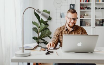 Best accounting software for e-commerce 2021 - man working on a laptop at a minimalist desk with a silver lamp and a green plant and bookcase in the background