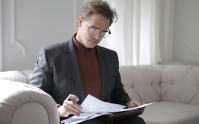 Most efficient way to pay yourself - man in a suit and polo neck with glasses sitting on a beige sofa in a minimalist room reading paperwork