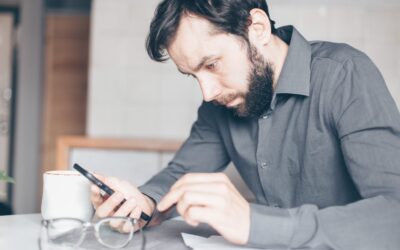 Square vs Stripe - Man in a grey shirt concentrating on his phone at a desk, glasses in the foreground